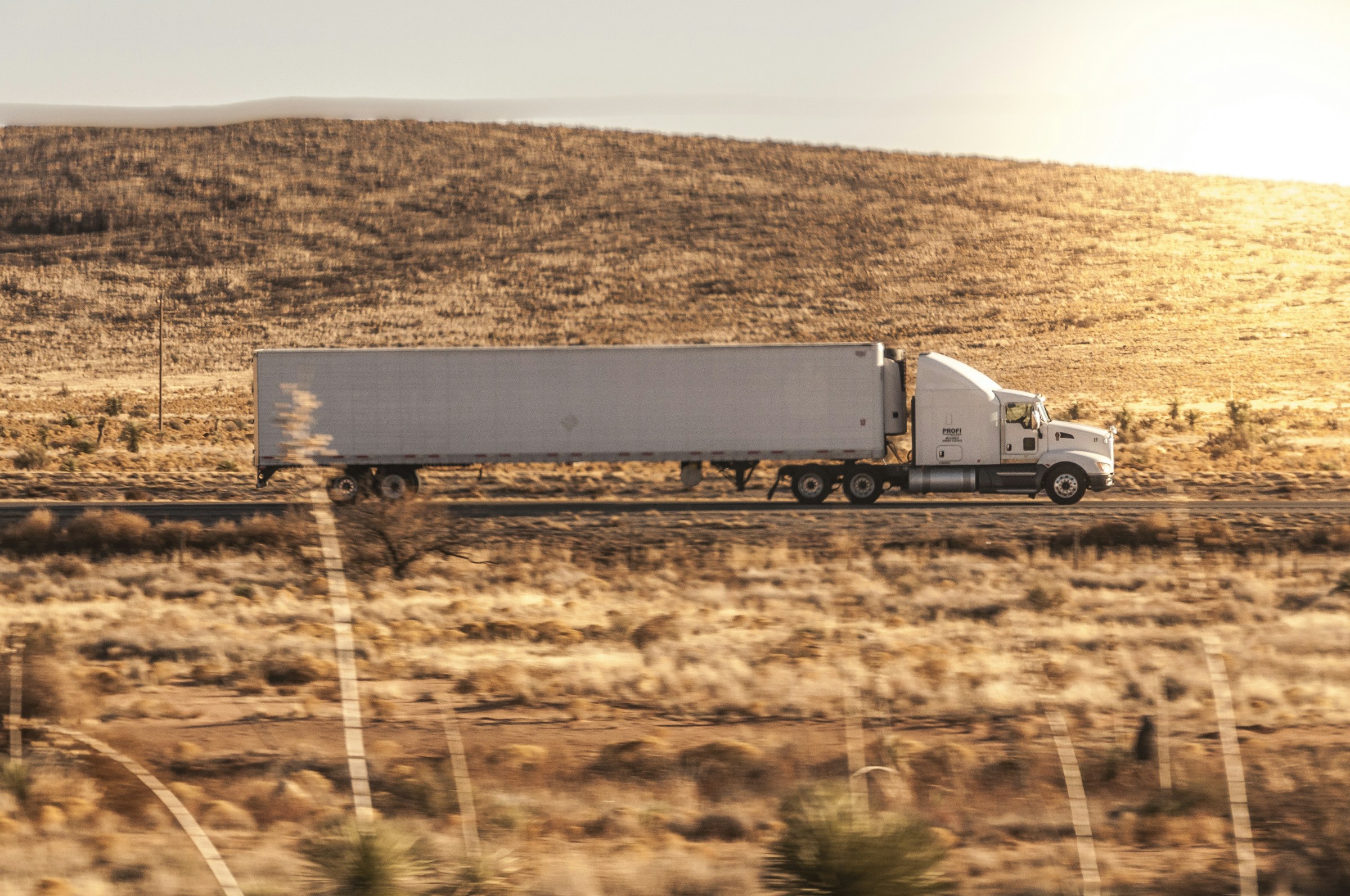 White semi truck crossing a sunlit western highway