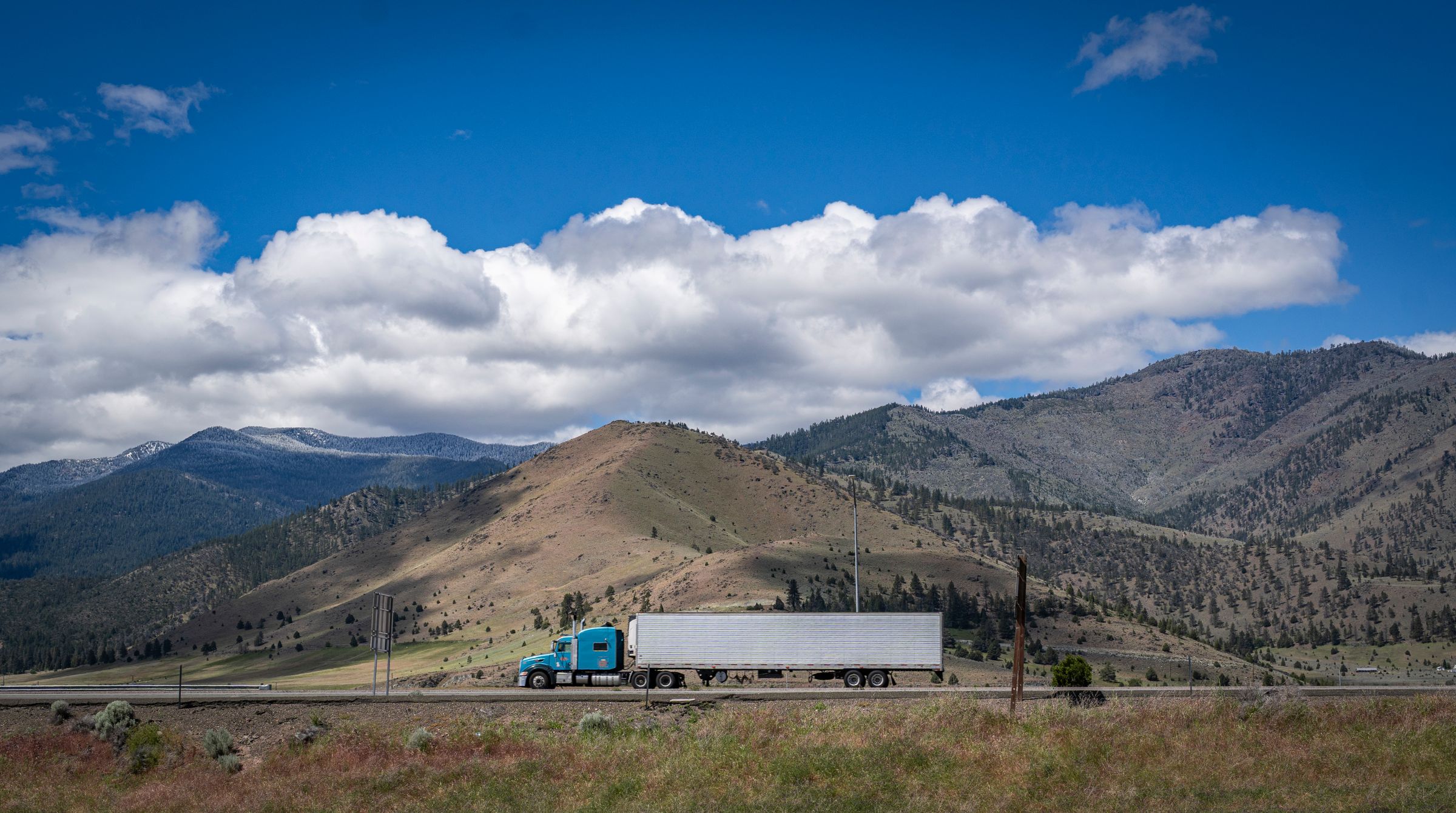 Blue semi truck crossing a scenic mountain highway
